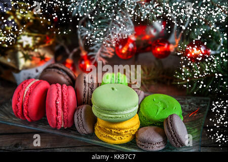 Fresh red macaroons at the Christmas table with the garland on the Christmas tree branches. Selective focus.. Snow. Stock Photo