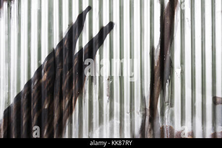 Texture of fence from corrugated iron. Graffiti detail. Silvery wall of wavy metal sheet sprayed with brown color. Close-up of pop art in urban street. Stock Photo
