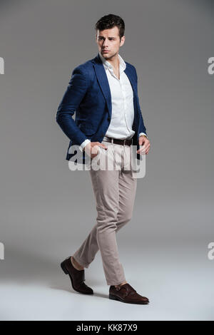 Full length portrait of a handsome serious man dressed in a jacket posing while standing and looking at camera isolated over gray background Stock Photo