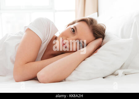 Photo of pretty cheerful young woman lies in bed at morning looking camera. Stock Photo