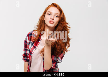 Picture of Pleased ginger woman in shirt sends air kiss at the camera over gray background Stock Photo