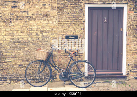 Vintage bicycle with retro wicker basket parked in front of a house front door. Matte finish. Stock Photo