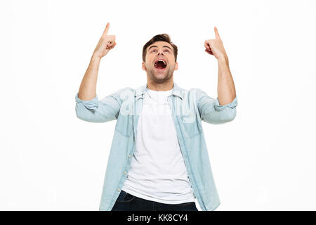Portrait of an excited young man standing and pointing two fingers up isolated over white background Stock Photo