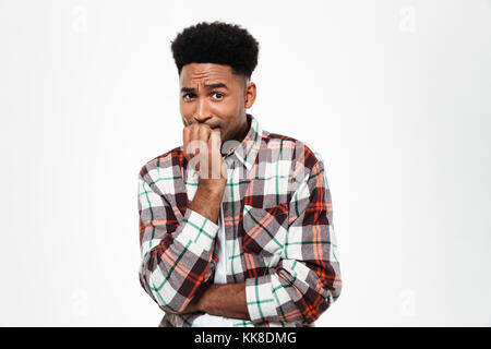 Portrait of a frightened young african man dressed in plaid shirt holding hand at his mouth and looking at camera isolated over white background Stock Photo