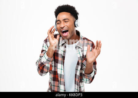 Portrait of a cheerful young afro american man listening to music with headphones and singing isolated over white background Stock Photo