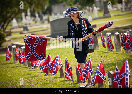 A member of the Daughters of the Confederacy removes Confederate flags on tombs of soldiers killed during the US Civil War at Magnolia Cemetery to mark Confederate Memorial Day on May 10, 2011 in Charleston, South Carolina.  South Carolina is one of three states that marks the day as a public holiday. Stock Photo