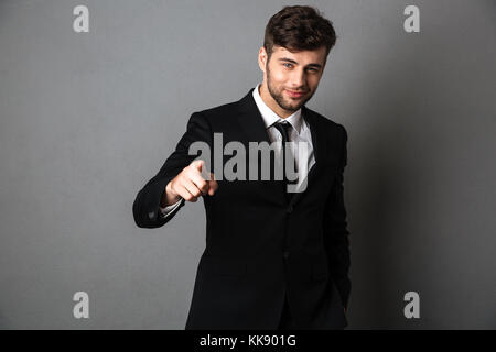 Young smiling man in formal wear pointing with finger on you, looking at camera, isolated on gray background Stock Photo