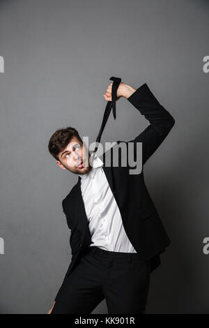 Desperate businessman strangling himself with a tie, isolated over gray background Stock Photo