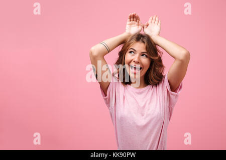 Photo of pretty cute young lady isolated over pink background posing gesturing with hands and looking aside. Stock Photo