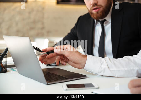 Cropped view of two business partners discussing new project while working with laptop in office Stock Photo