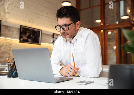Cheerful unshaven businessman in white shirt looking at laptop screen in office Stock Photo