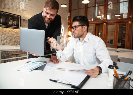 Portrait of a two businessmen discussing an issue while using laptop computer at a workplace Stock Photo