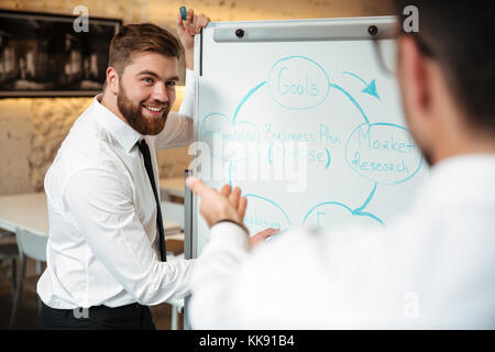 Two young businessmen having a meeting and discussing business plan on a blackboard indoors Stock Photo