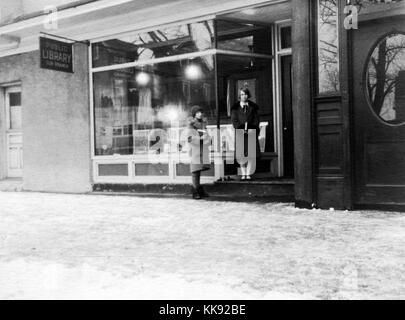 An exterior photograph of the New Dorp Library, it began as a community library and became a sub-branch of the New York Public in 1926, two young women are holding books while waiting outside of the library, the ground has a covering of snow, 1926. From the New York Public Library. Stock Photo