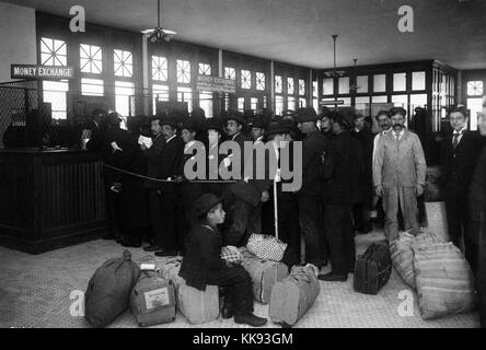 Black and white photograph of a large group of immigrants with baggage lined up at tellers windows marked 'Mone Exchange', by Edwin Levick, Ellis Island, New York, 1907. From the New York Public Library. Stock Photo