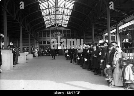 Black and white photograph of a large group of immigrants lined up outside waiting to be taken off Ellis Island, by Edwin Levick, Ellis Island, New York, 1907. From the New York Public Library. Stock Photo