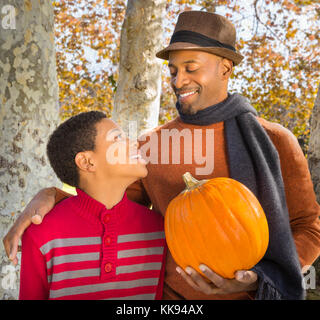 Togetherness. Waist up portrait of Handsome African-American hipster father and happy son spending time together and choosing a pumpkin. Park or count Stock Photo