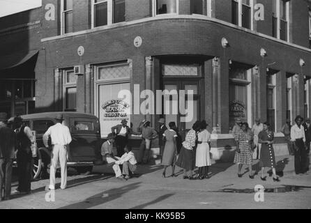 Black and white photographof a large group of African-American people standing and walking in front of a bank on a Saturday afternoon, Lexington, Holmes County, Mississippi Delta, October, 1939. From the New York Public Library. Stock Photo
