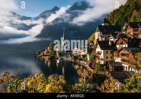 Scenic view of famous Hallstatt lakeside town reflecting in Hallstattersee lake in the Austrian Alps in morning light in autumn with bushes and flower Stock Photo