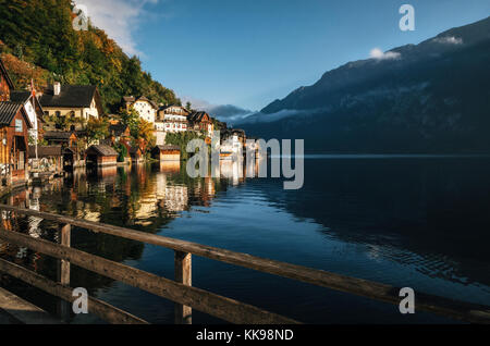 Scenic view of famous Hallstatt lakeside town reflecting in Hallstattersee lake in the Austrian Alps in morning light in autumn with fence on the fore Stock Photo