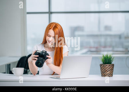 redhead woman looking at camera while working on laptop Stock Photo