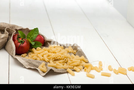 pasta and tomatoes in a tissue and scattered on a white old wooden boards Stock Photo