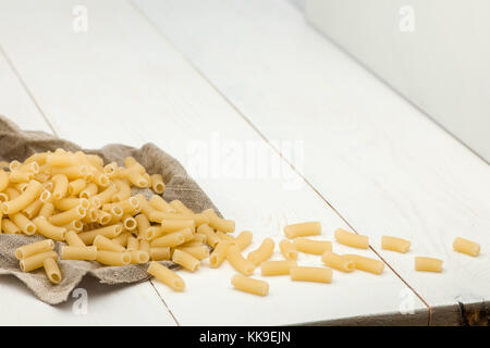 Scattered pasta in white cloth on a white old wooden boards Stock Photo