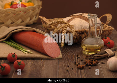 sausage and bread in a wicker basket and vegetables and garlic on a table Stock Photo