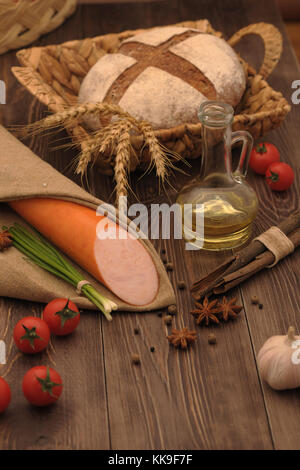 sausage and bread in a wicker basket and vegetables and garlic on a table Stock Photo