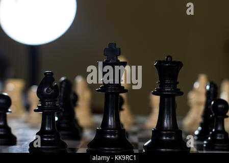 king queen and bishop close up on a chessboard and a single light above from behind Stock Photo