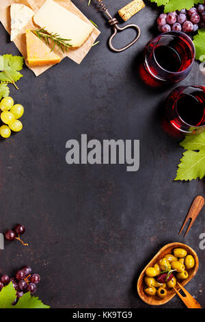 Wine and snack set. Variety of cheese, mediterranean olives, black and green grapes and glasses of red wine over dark background, top view, copy space Stock Photo