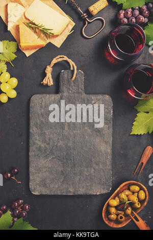 Wine and snack set. Variety of cheese, mediterranean olives, black and green grapes and glasses of red wine over dark background, top view, copy space Stock Photo