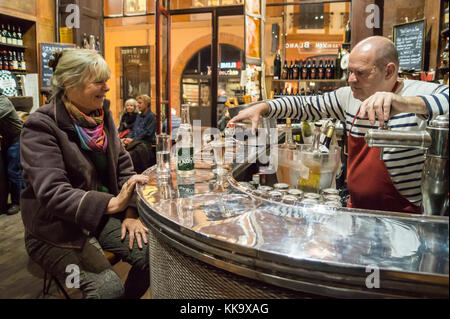 Barman pouring quinquina aperitif for a seated woman, Au Père Louis bar restaurant interior,  Rue des Tourneurs, Toulouse, Occitanie, France Stock Photo