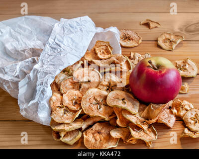 Dried apples poured from a paper bag on the table top is a fresh red ripe juicy apple Stock Photo