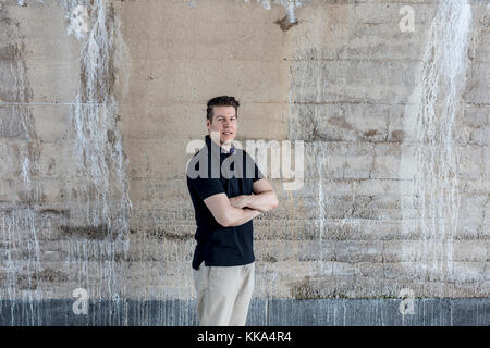 A casually dressed man standing behind a beige colored wall. Three quarters length. Stock Photo