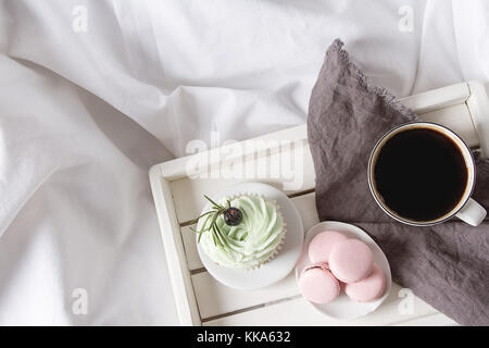 Muffins or capkakes with pistachio cream with macaroons and black coffee on a wooden tray in bed. White background. Sweet food. Festive mood Stock Photo