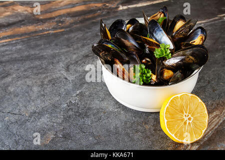 Mussels with herbs in a white bowl with lemon. Seafood. Food at the shore of the French Sea. Dark background Stock Photo