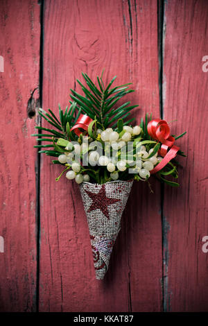 closeup of a bunch of mistletoe wrapped in a festive fabric, on a red rustic wooden surface Stock Photo
