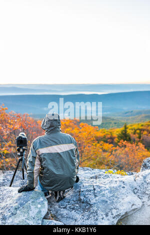 Sitting young man photographer with camera, gear, and tripod on cold autumn morning in jacket in Bear Rocks, West Virginia taking pictures of sunrise Stock Photo