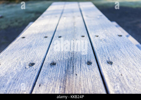 White frost ice crystals on wooden picnic table in morning sunlight macro closeup with shiny sparkling bokeh Stock Photo