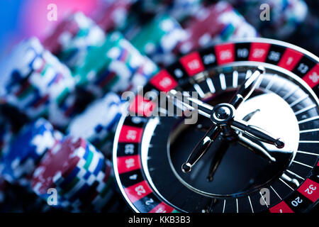 Casino theme. High contrast image of casino roulette, poker game, dice game, poker chips on a gaming table, all on colorful bokeh background. Stock Photo