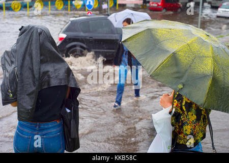 Women crossing flooded urban road in the heavy rain Stock Photo