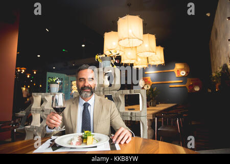 Handsome middle-aged businessman having lunch and drinking red wine in restaurant Stock Photo
