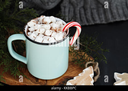 Enamel cup of hot cocoa drink with marshmallows and candy cane against a rustic background with beautiful wood Christmas tree ornaments and a grey sca Stock Photo