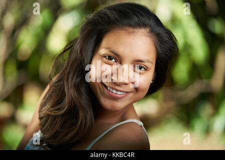 Attractive smiling young hispanic woman headshot portrait on natural background without makeup Stock Photo