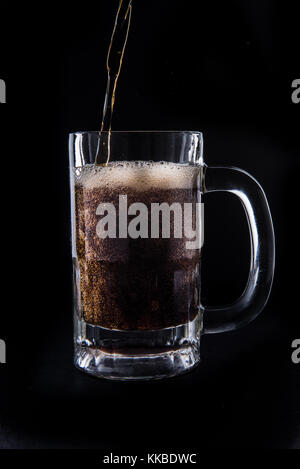 Cola being poured into a mug on an isolated black background. Stock Photo