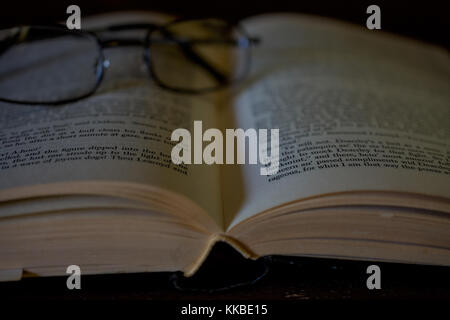 A pair of reading glasses resting on an old open Kiplling book,  suggesting an elderly person taking a break from reading Stock Photo