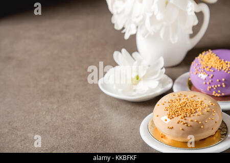 Fashionable mousse cake with a mirror glaze decorated with spring flowers. Dark background. Stock Photo