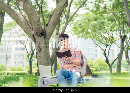 Young asian man with backpack reading a book Stock Photo