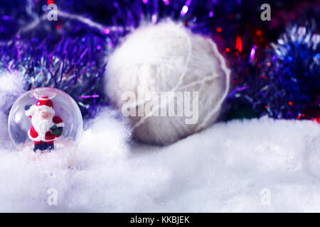 Christmas and new year background with santa claus in glass ball, white yarn on soft defocused snowy background with tinsel. Stock Photo